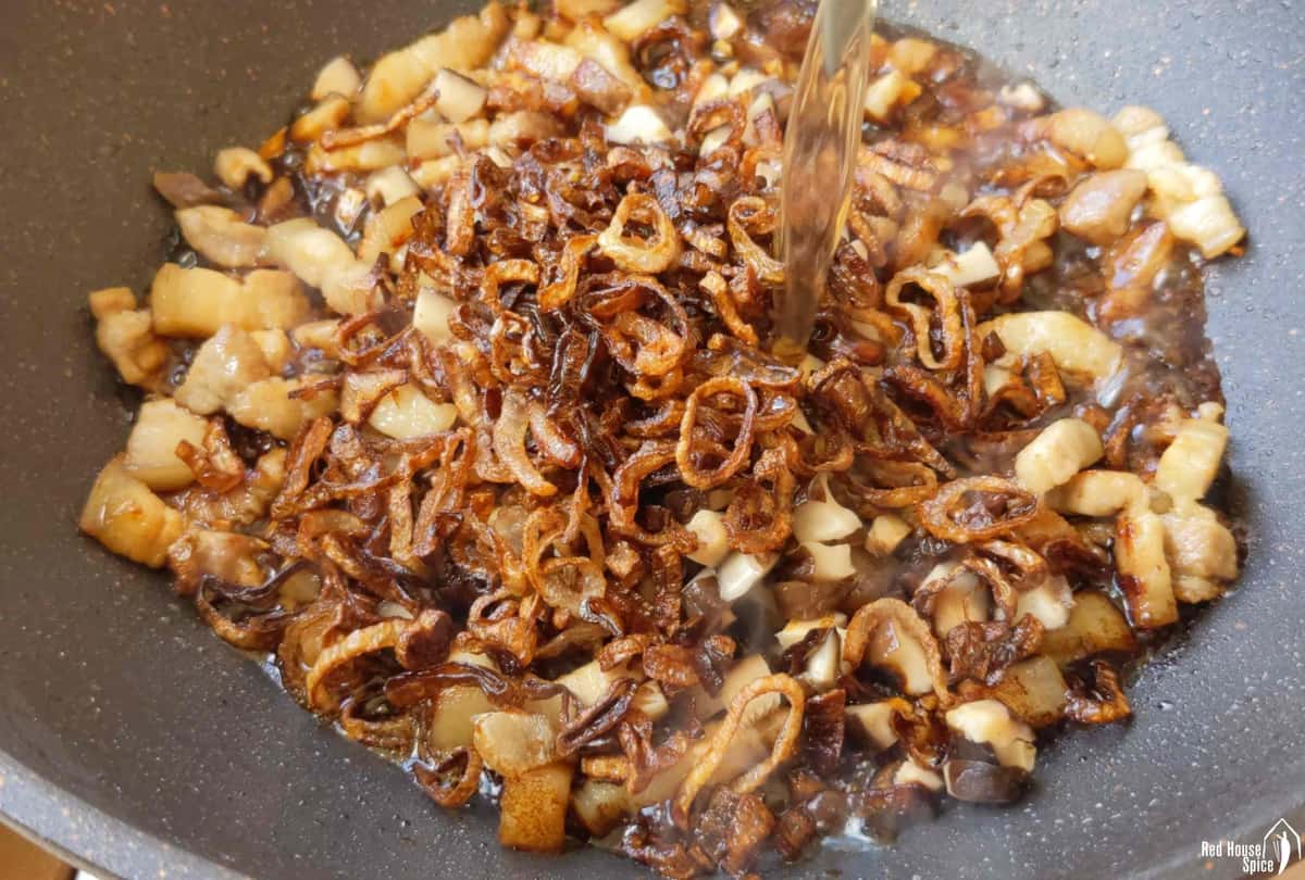 pouring water into a wok with pork and crispy shallots.