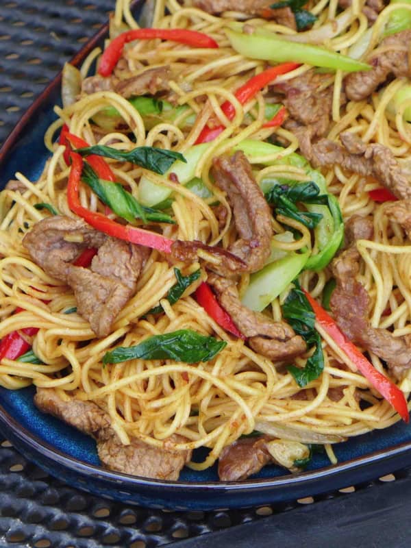 a plate of beef chow mein with sha cha sauce.