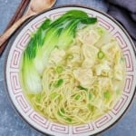 a bowl of wonton noodle soup with bok choy.