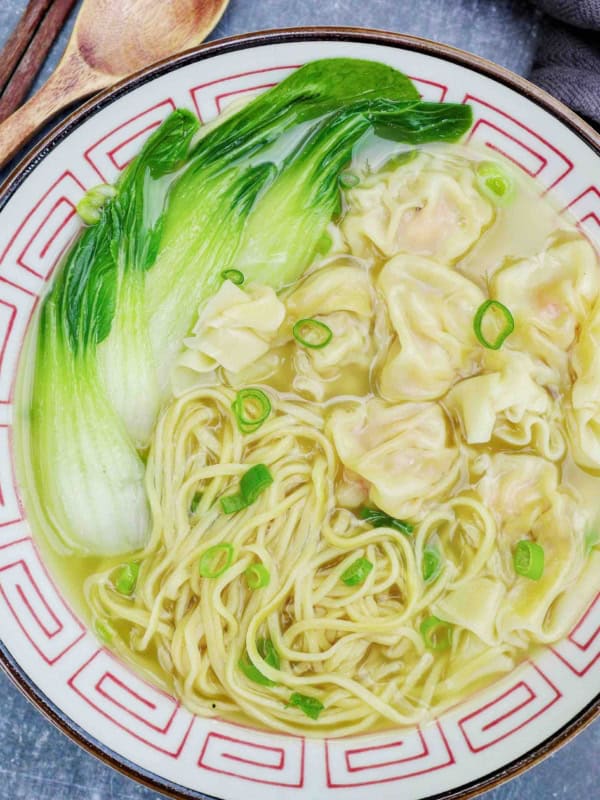a bowl of wonton noodle soup with bok choy.