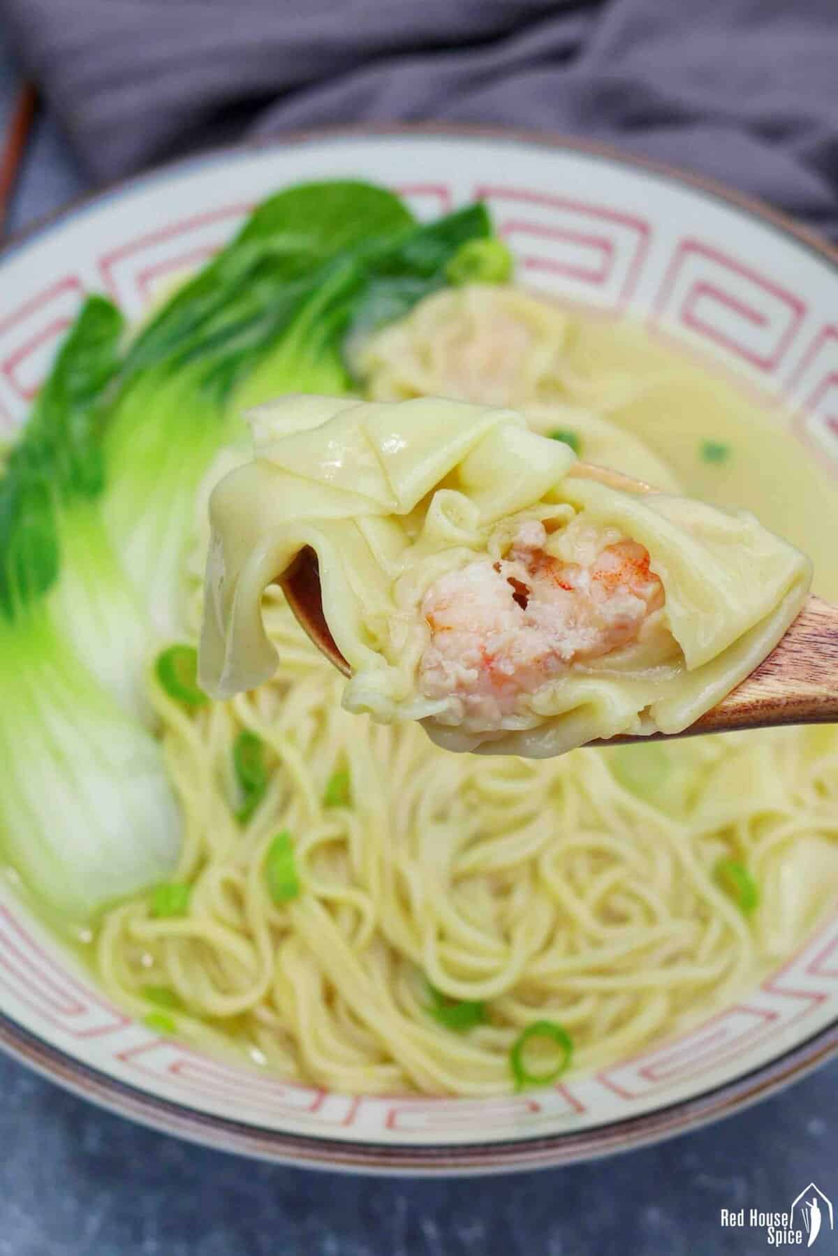 a half-eaten wonton held by a spoon.
