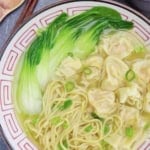 a bowl of wonton noodle soup with bok choy.