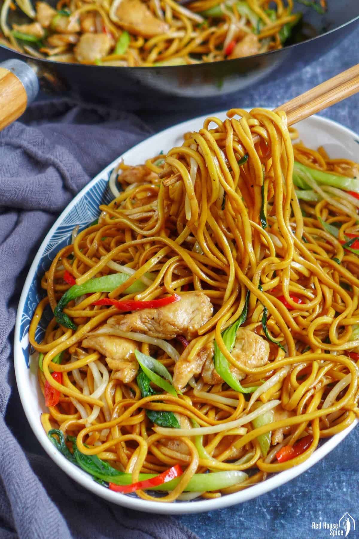 Chopsticks lifting up chow mein noodles.