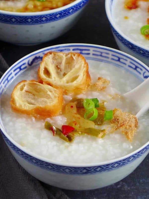 a bowl of plain congee with toppings like fried dough, preserved mustard stem and pork floss