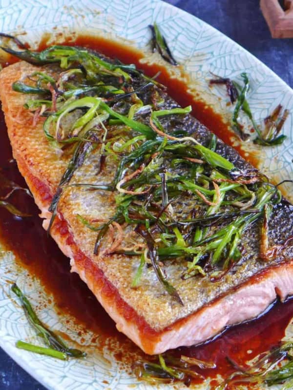 Cooked salmon filet over a dark sauce and topped with fried scallions and ginger.