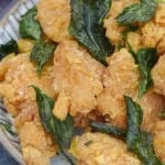 a plate of popcorn chicken with fried basil leaves.