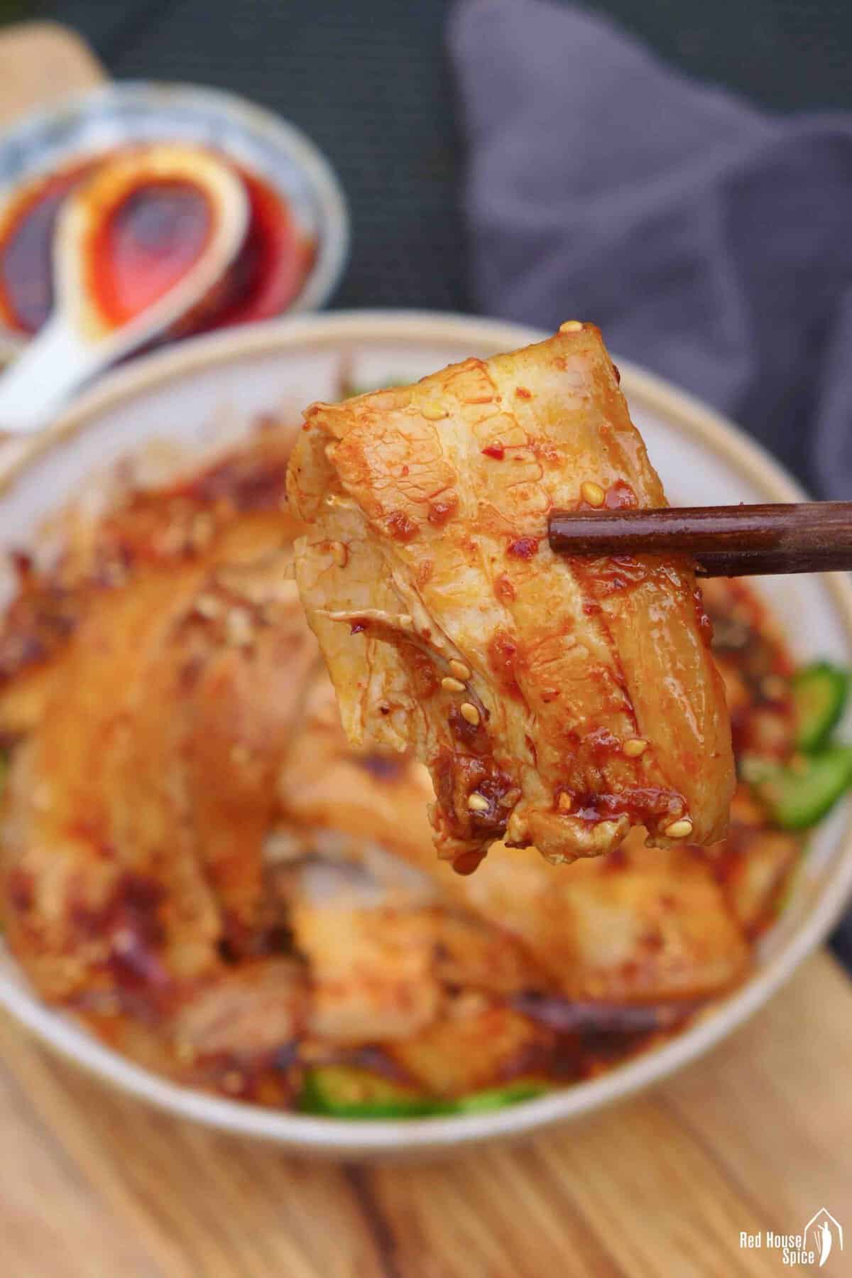 chopsticks picking up a piece of pork belly.