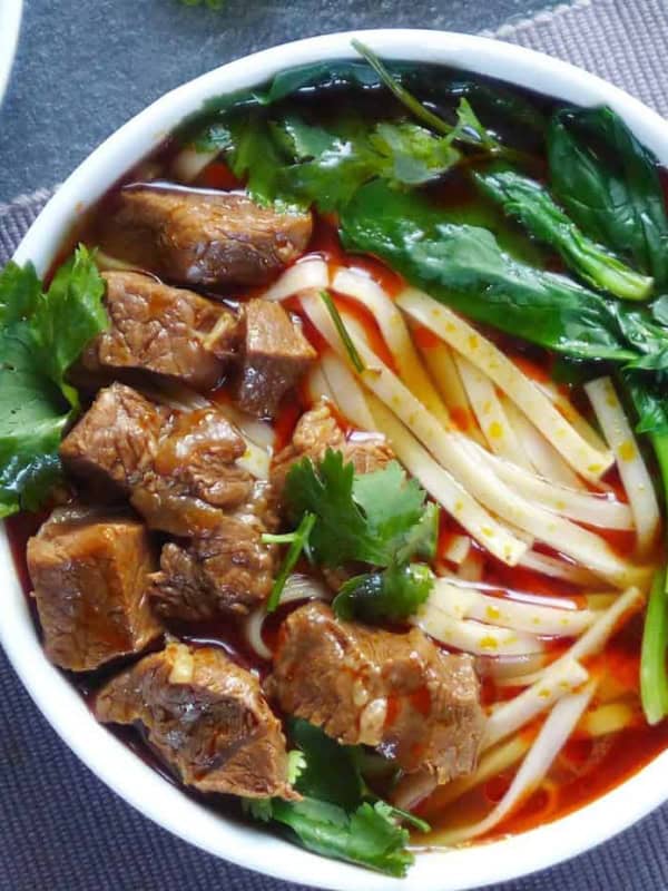 A bowl of noodle soup topped with beef cubes