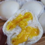 A halved custard bun held by a hand with overlay text that says Steamed custard buns