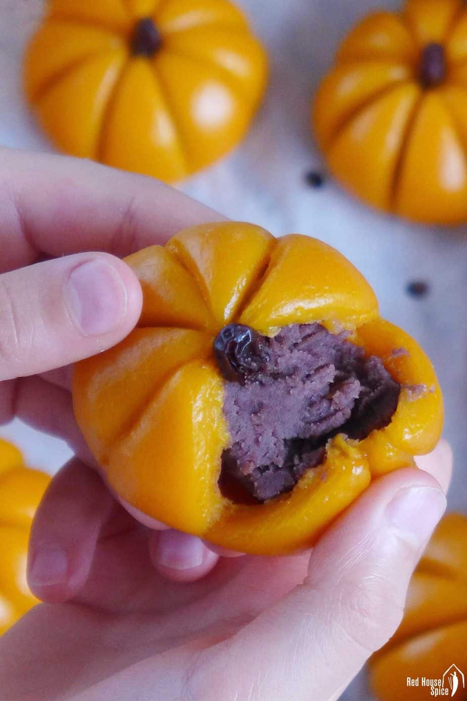 A pumpkin mochi cake torn open showing its red bean paste filling.